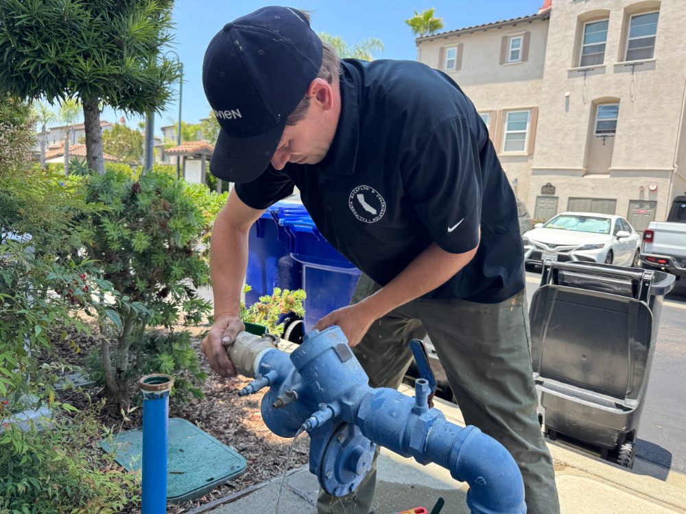 California Backflow & Chlorination technician testing a blue backflow preventer in a residential neighborhood